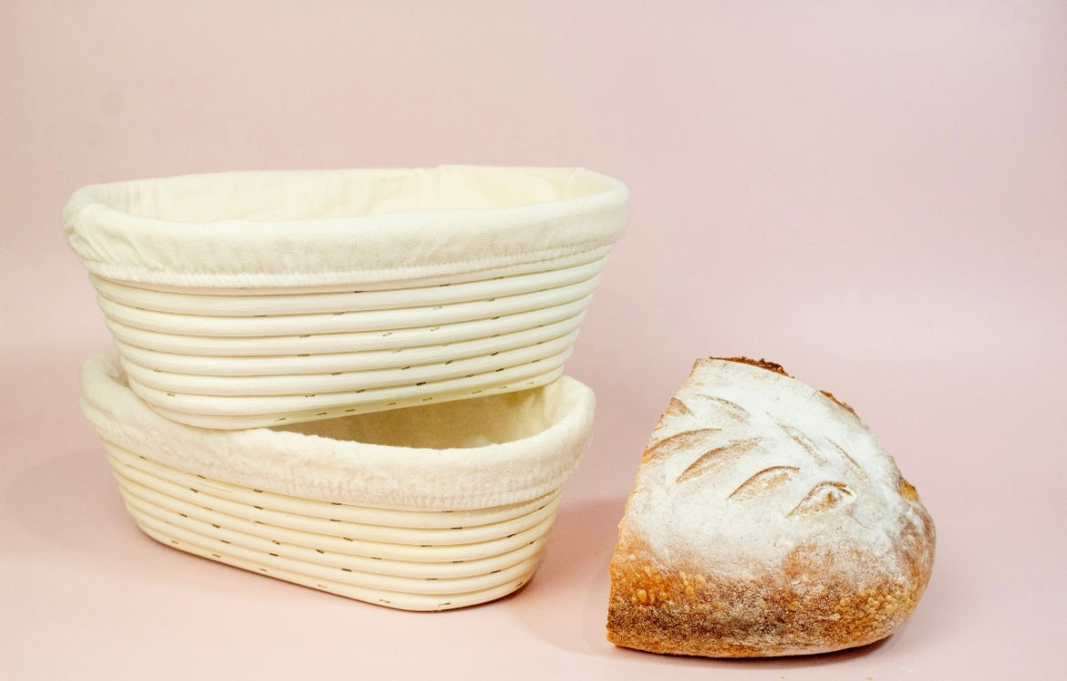 Two woven bread baskets and a loaf of bread on a pink background